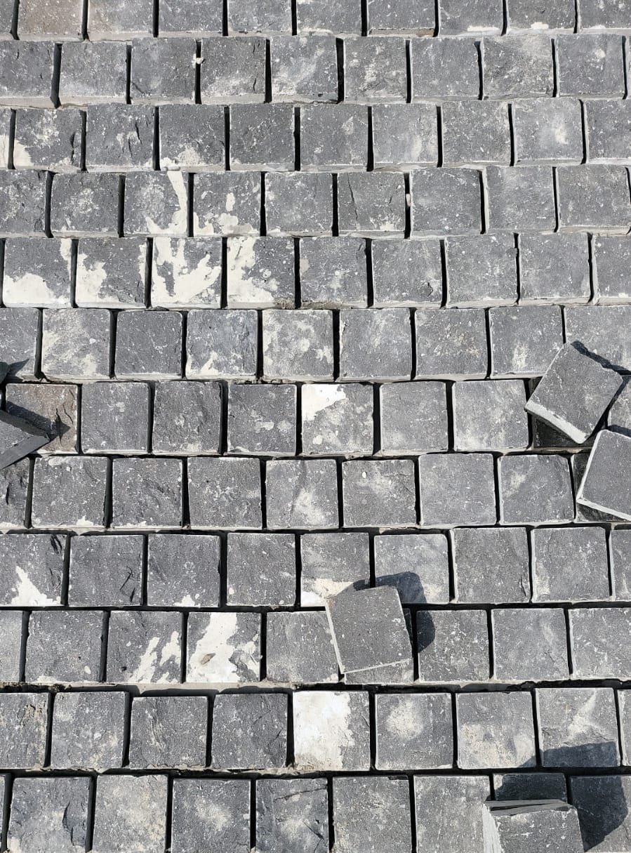 Rows of split face basalt cobbles with sawn edges laid in running bond on a mortar bed, with loose cobbles waiting to be set, at a house in Fazilka, Punjab