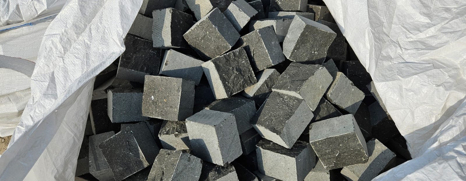Split face black basalt cobbles in a white jumbo bag, showing smooth machine-sawn sides and rough natural split tops